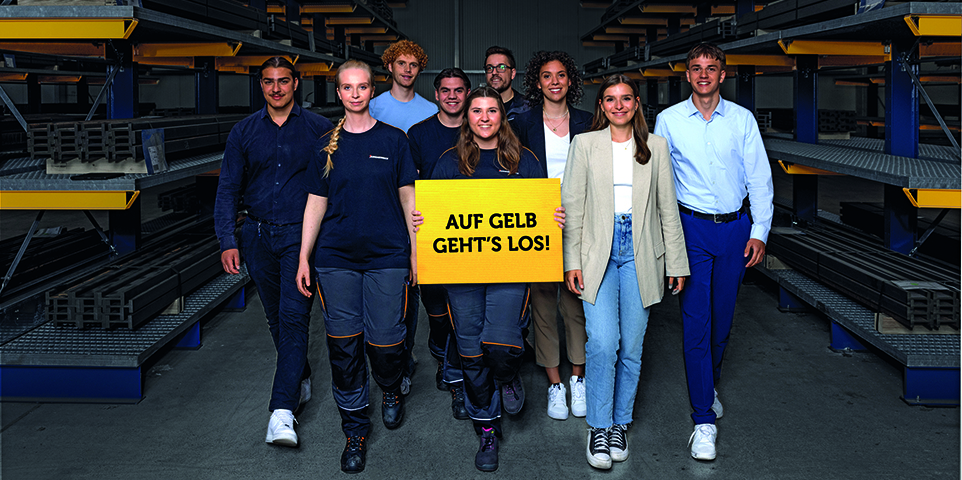 Gruppe junger Menschen läuft durch Werkshalle auf Kamera zu. Mädchen in der Mitte hält ein gelbes Schild mit der Aufschrift "AUF GELB GEHT'S LOS!" hoch