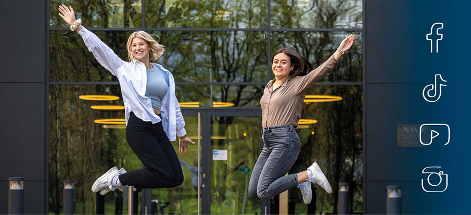 Zwei Azubis springen vor dem Gebäude der Nordwest Mediengruppe in die Höhe. 