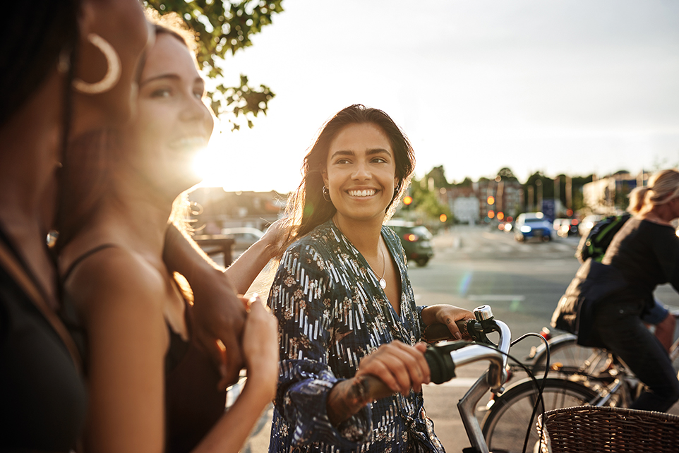 Junge Frau schiebt Fahrrad und unterhält sich mit anderen jungen Leuten