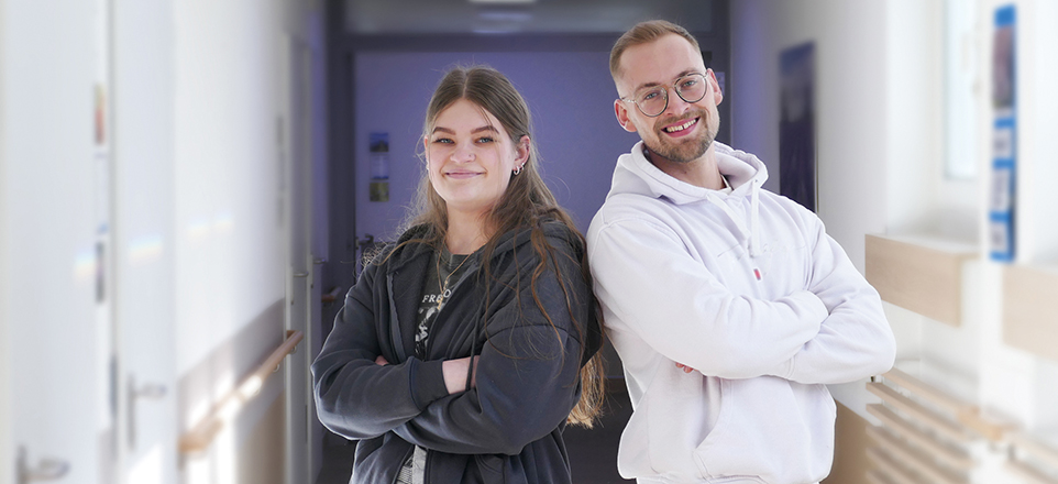 Zwei junge Menschen im Flur lachen in die Kamera