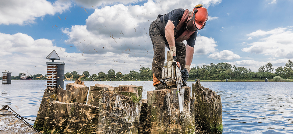 Mann mit Helm zersägt Baumstamm am Fluss