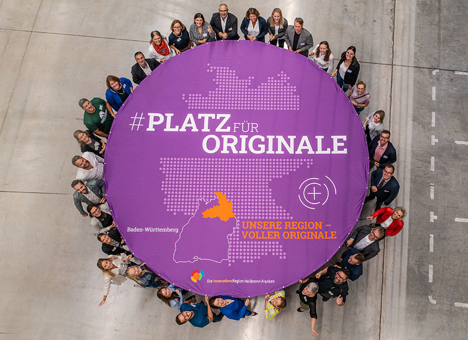 Gruppe von Personen hält ein rundes Banner #PLATZ FÜR ORIGINALE