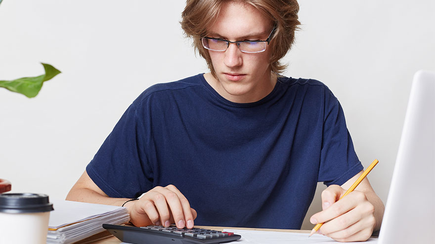 Junger Mann sitzt mit Taschenrechner am Schreibtisch. Bild von user18526052 auf Freepik.